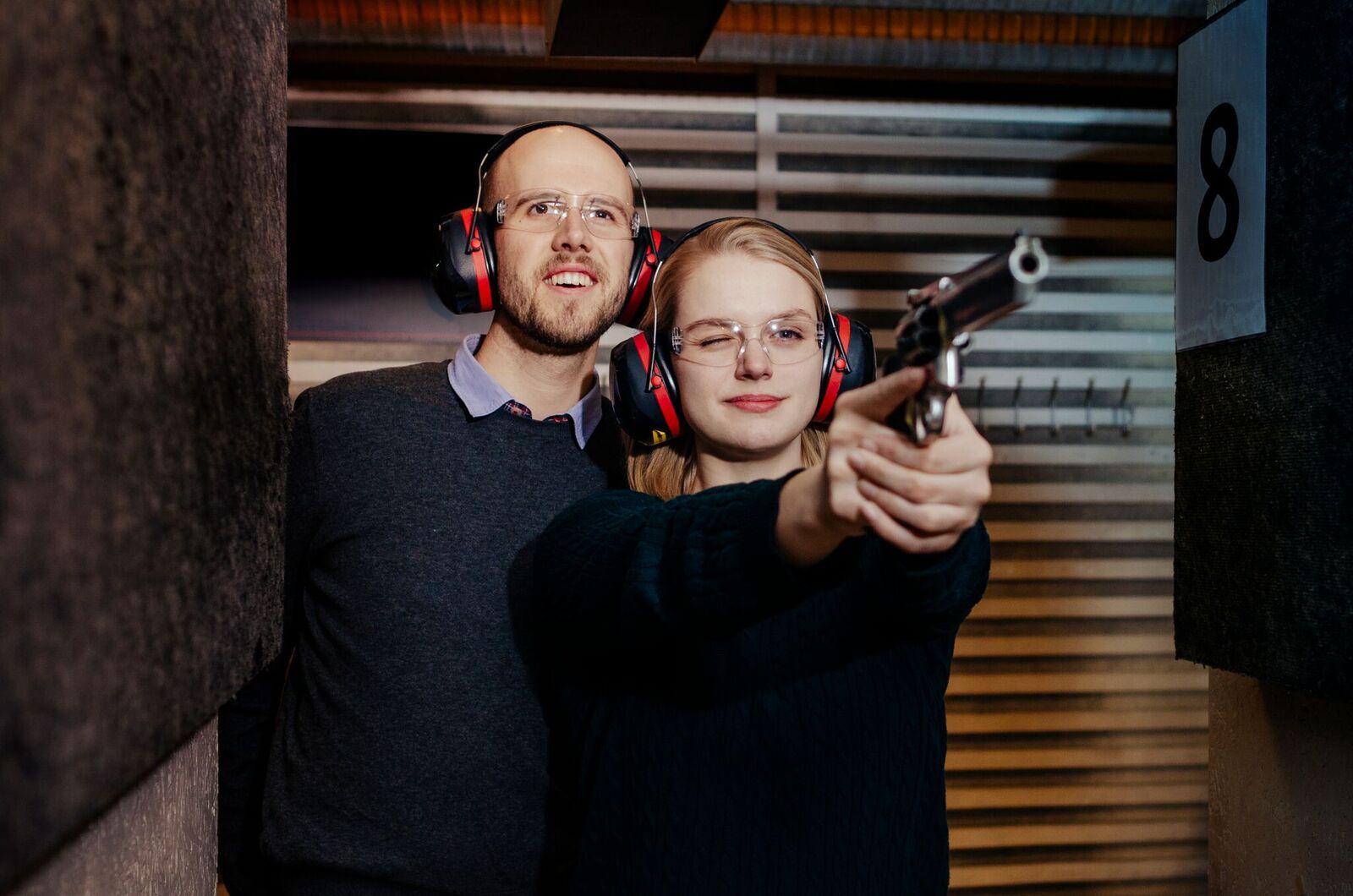 En dame som sikter med en pistol med kjæresten som står bak og følger spent med. Leter du etter julegaver til han som har alt, er dette et godt alternativ.