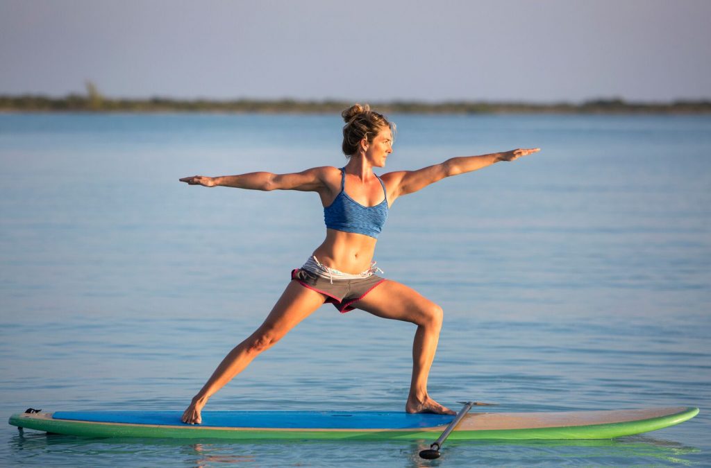 Ung jente som gjør yoga på et surfebrett på vannet. Hun strekker armene ut fra kroppen og ser veldig fredfull ut. En gave til venninne som vil bli husket!