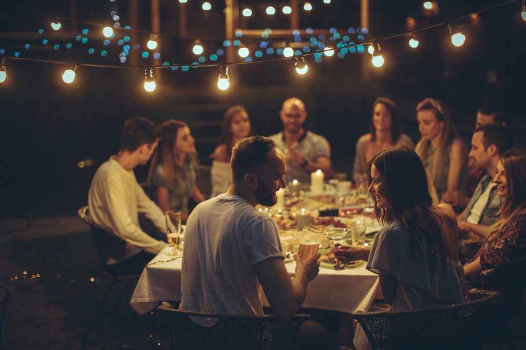 Bilde av glad vennegjeng som spiser middag rundt et stort bord. Perfekt innflytningsgave - tips finner du her.