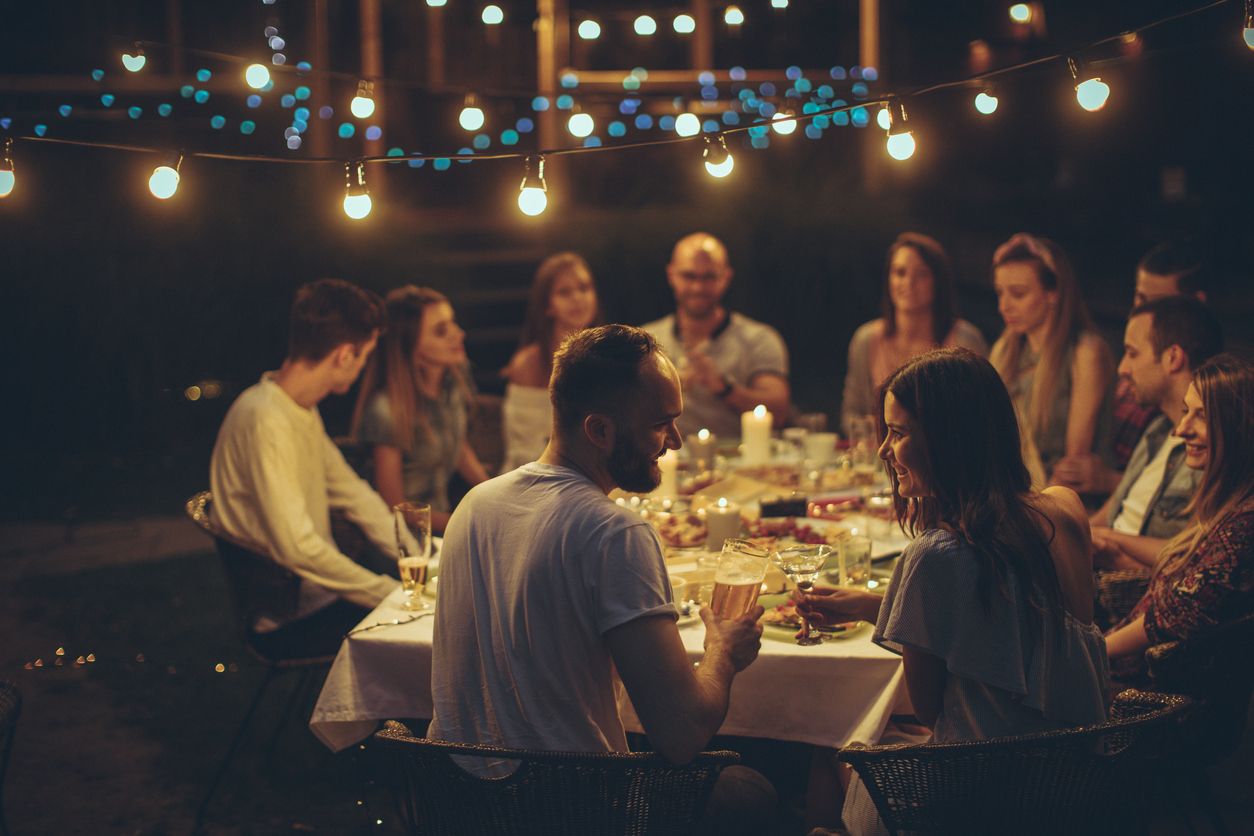 Bilde av glad vennegjeng som spiser middag rundt et stort bord. Perfekt gave til vertinne.