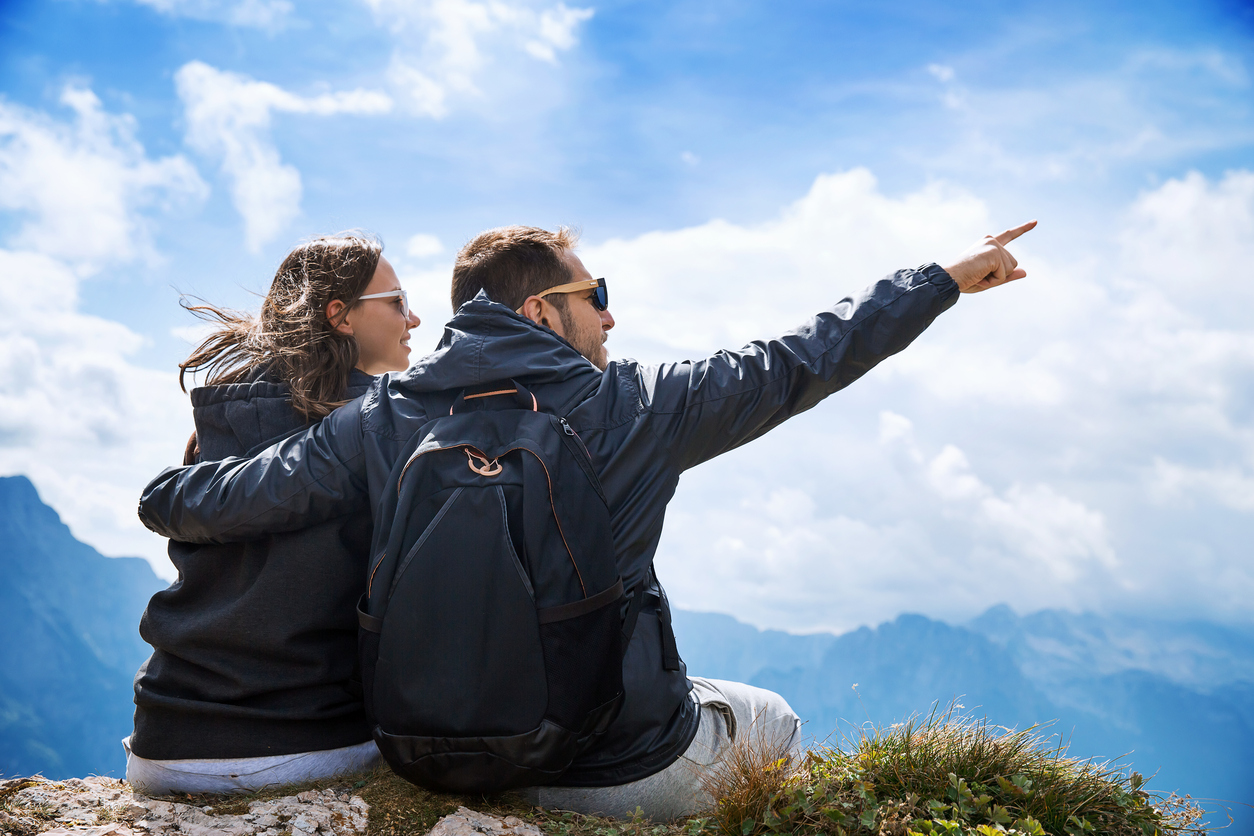 Par på toppen av fjell som holder rundt hverandre og peker mot utsikten. Kjærestetur sommer 2017.